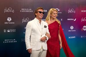 Valeria Mazza y Alejandro Gravier en la alfombra azul de los Premios Platino 2026. La top model argentina luce un vestido de lentejuelas carmesí de un solo hombro con capa fluida, y su esposo viste un esmoquin negro clásico.
