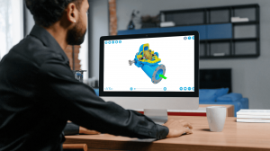 Man viewing 3D blue and yellow pump CAD model on computer screen at office desk.