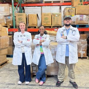 Ava with Two Other Individuals Standing In Front of the 15,000 STEAM Products to Be Distributed for the Fuel The Future Donation Drive