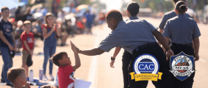 Police officer giving a high-five to a child at an outdoor community event with bystanders in the background.