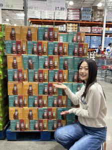ginsa founder Juliet Kim Blake posing beside a Costco display of the brand’s sparkling Korean ginseng tonic variety packs.