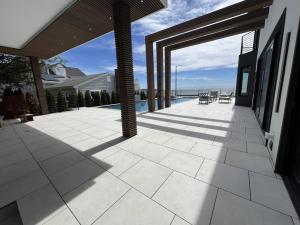 Luxury pool deck installation by Backyard Experts in Massachusetts, featuring large-format porcelain pavers, a custom wood-slat pergola, modern cable railing, and waterfront outdoor living space.