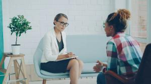 Clinician in white blazer taking notes during a therapy session with a client, representing the individualized clinical work at Asana Recovery's LGBTQ+ specialty program in Orange County.