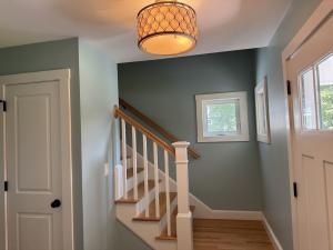 Interior painting and staircase trim project by Marcos Painting in Nashua, New Hampshire, featuring a residential foyer with sage green accent walls, custom white stair balusters and newel post, hardwood treads, and professional door and window trim finis