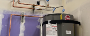 A professional installation of a Rheem water heater secured with earthquake straps, featuring precision-installed copper water lines and shut-off valves by KPS Plumbing.