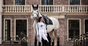Royal Equestrian woman in white luxury riding outfit beside grey horse at historic European estate