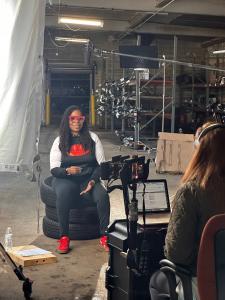 Natasha Broxton being interviewed by Google’s camera crew while sitting on stacked tires inside Select Auto Parts & Sales, a Milwaukee auto recycling facility featured in Google’s Portraits of AI campaign.