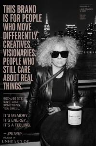 Portrait of Britney Ferguson, founder of Unheard Of, wearing sunglasses and a black leather jacket with the New York City skyline at night. In the foreground, the Heaven’s Pearl luxury candle is lit on a table.