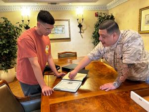 Marcelo Umanzor Blanco pointing to a certificate of formation in a professional binder while reviewing business documents with a young entrepreneur.