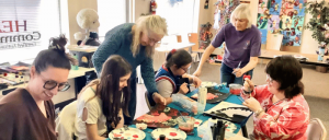 A group of people gathered around a table, painting colorful artworks together in a bright, creative room.