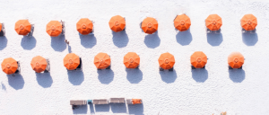 Aerial view of a sandy beach with two rows of orange umbrellas and sunbeds casting long shadows on the white sand.