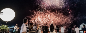A crowd of guests captures photos of a vibrant fireworks display lighting up the night sky from a luxury viewing deck at the f1 singapore Grand Prix