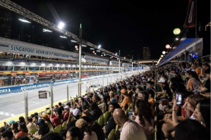A crowded Pit Grandstand overlooks the brightly lit Marina Bay Street Circuit and pit buildings during the f1 singapore night race.