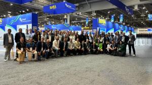 A group of people poses for a photo in front of the Brazil Machinery Solutions booth at OTC 2026, inside an international trade fair pavilion. The participants are arranged in two rows, with some standing in the back and others crouching or seated in the 