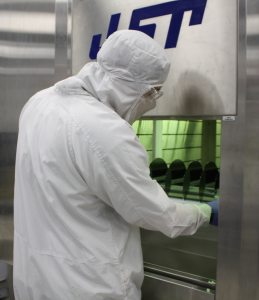 Person in a white fab suit standing in front of a tray of semiconductor wafers in a JST system