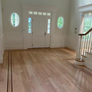 Newly installed hardwood floors in a Greater Boston entryway by GB Hardwood Floor Inc, featuring natural wood finish and decorative border inlay.