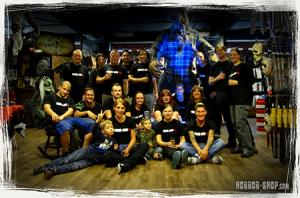 Teamfoto von Horror-Shop.com im Showroom mit Halloween-Dekoration, Kostümen, Requisiten und einer großen Monsterfigur im Hintergrund.