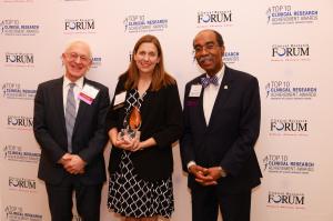 Two men in suites are standing on either side of a woman in a dress.  From left to right, the people are Dr. Harry Selker, Clinical Research Forum chair, Dr. Rebecca Ahrens-Nicklas, who is holding a statuette award, and Dr. E. Albert Reece, Clinical Resea