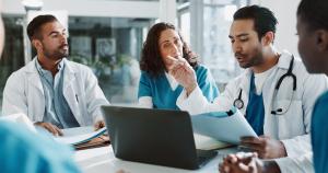 photo of a team of health professionals seated at a conference table around the leader who has a lap top and is presenting on a topic to the group