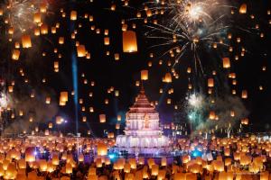 A brightly lit white pagoda surrounded by thousands of floating sky lanterns and exploding fireworks during the Chiang Mai CAD Yi Peng Festival.