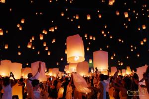 Festival participants releasing glowing paper sky lanterns into the dark night sky at the Chiang Mai CAD Yi Peng Festival.