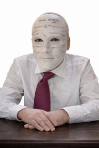 Retrato de Ronee Hulk sentado frente a una mesa usando una máscara blanca con fórmulas matemáticas y referencias a inteligencia artificial impresas sobre ella.