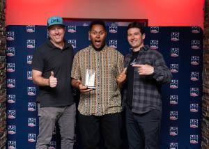 The males holding an award in front in front of a backdrop with the US Ski & Snowboard logo on it.
