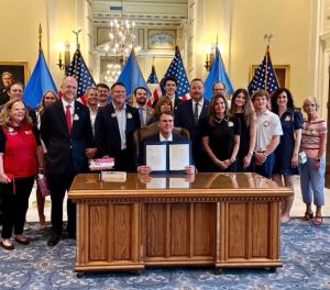 Oklahoma Governor Kevin Stitt signs the Blake Burgess Blood Clot Prevention Act into law on May 18, 2026, surrounded by members of the Burgess family, representatives from the National Blood Clot Alliance, advocates, and lawmakers.
