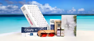 FlyWell wellness programme products displayed on a sandy beach, featuring a Vital Red Light therapy panel, Firefly recovery device, amber-tinted glasses, Life Tune device, wellness supplements, and the FlyWell branded booklet against a turquoise ocean bac