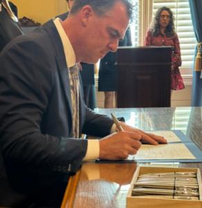 Governor Kevin Stitt wearing a suit and signing his name