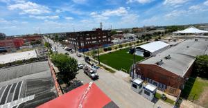 High angle view of the FIFA Fan Festival site under construction in EaDo, Houston, with tents, nearby streets, warehouses, and a bright blue sky.
