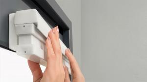 Close-up of a person's hands effortlessly installing a white, cordless cellular shade onto a dark window frame using a no-tool magnetic mounting system.