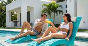 AquaCurve in-pool loungers on a shallow sun shelf with two people relaxing in a backyard pool.