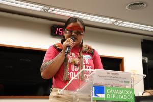 A woman wearing traditional face paint speaks into a microphone.
