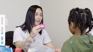 A Bierman Autism Centers speech-language clinician holds up a small toy basket while working with a young child during a play-based therapy session.