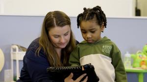 A Bierman Autism Centers clinician and a young child look together at a tablet during a one-on-one therapy session.