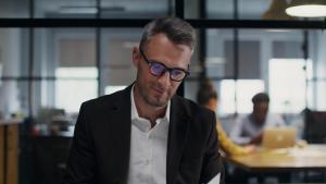 Professional wearing a suit and glasses glances at offscreen tech device. Seems to have received good news.