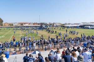 Wide view of Dallas Cowboys training camp in Oxnard, California, at Ventura County Coast, featuring players scrimmaging on multiple fields with large crowds of fans watching from the stands.