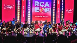 RCA students kneeling onstage in front of a bright pink and red backdrop as part of a welcome performance for NFF’s staff.