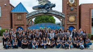 NFF staff lined up for a photo in front of the entrance to RCA, which has large brick columns and a blue tile gate with a dragon sculpture on top.