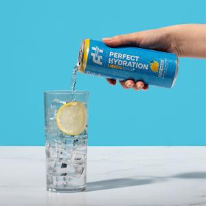 Perfect Hydration Lemon Flavored Alkaline Water being poured from blue can into clear glass with ice and lemon. Super refreshing clear liquid without carbonation