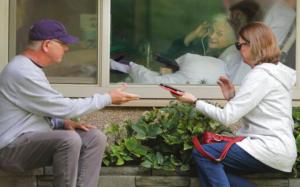 Man and woman visit with elderly relative through window.