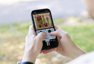Someone playing games on their phone with a Playtiles controller stick on the screen.