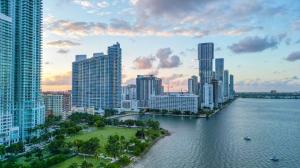 Aerial view of the Miami Brickell waterfront skyline with modern residential high-rise buildings along Biscayne Bay at sunset.