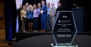 The Crisis Jam's 2026 AAS Crisis Services Innovation Award is in the foreground while the Crisis Jam Founders and Partners are in the background on stage.