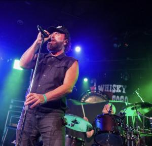Brad Henshaw performing live on stage with microphone and concert lighting.