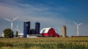 An Iowa corn farm with tall Pocfarmer silos, a red barn, and several wind turbines, illustrating high-yield and eco-friendly farming practices.