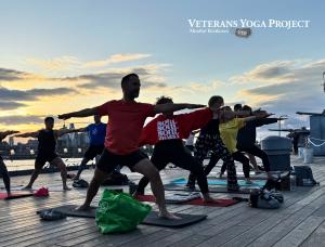 Veterans in warrior 2 pose are practicing yoga on the deck of the Battleship New Jersey at sunset