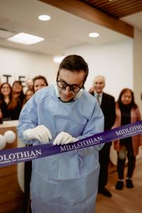 Dr. Sobti makes the intitial incision to the ceremonial ribbon while wearing a surgeon's gown and surgical loupes