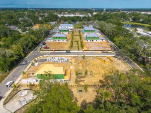 Aerial drone view of Lakeview Village construction site in Winter Garden, Florida, with multiple townhome buildings framed and single-family home foundations underway, surrounded by mature trees.